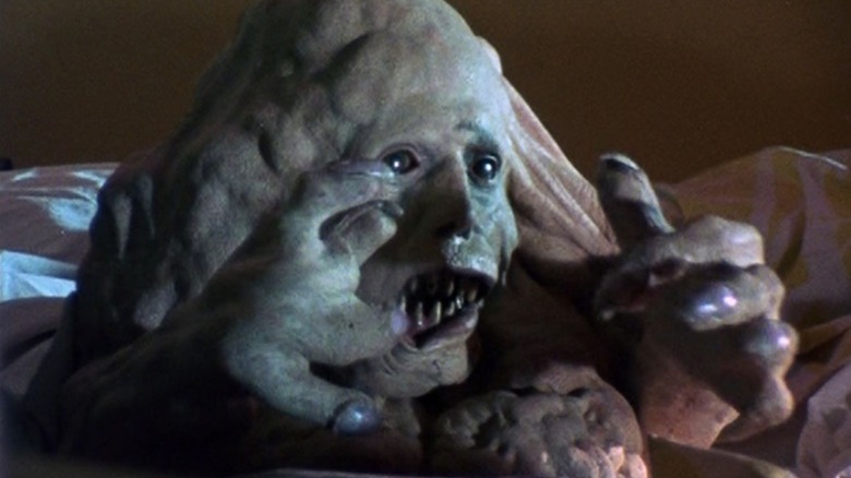 The grotesque, monstrous blob of flesh Belial in Basket Case, sitting there with his fangs and distorted hands while looking ahead at something.
