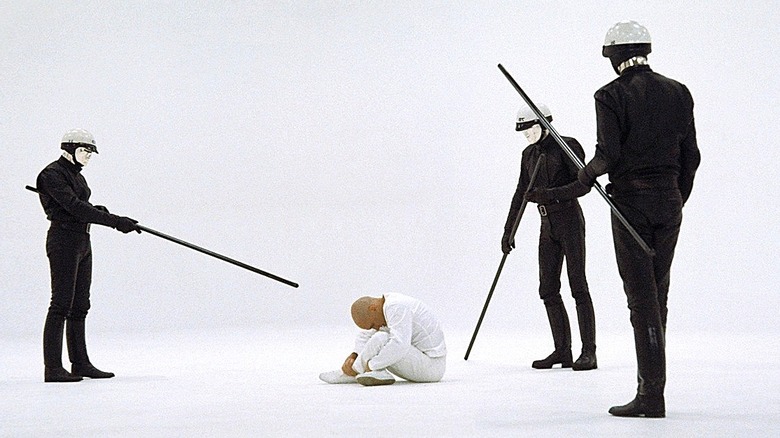 Robert Duvall as THX 1138 in THX 1138, sitting on the floor while being intimidated by the black-clad android police officers.