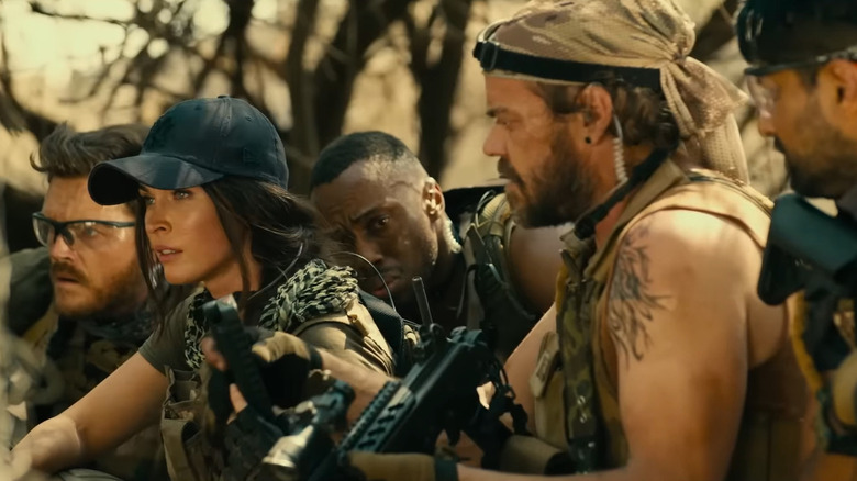 Megan Fox as Sam dressed in military gear surrounded by men with machine guns in Rogue