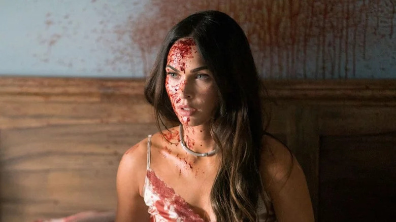 Megan Fox as Emma sitting on bed with blood splattered on her face and the walls in Till Death