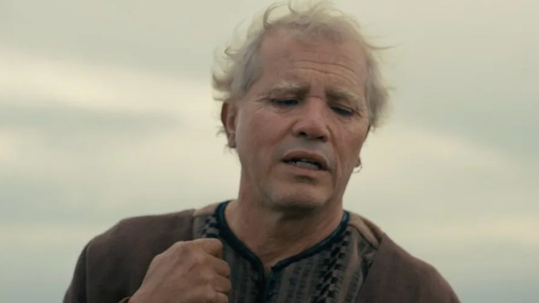 A medium shot of John Leguizamo as Eumaeus in The Odyssey, backgrounded by the overcast sky.