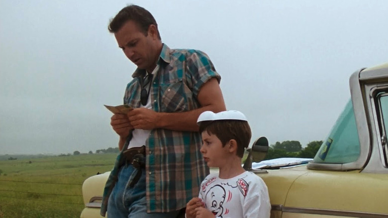Kevin Costner as Robert "Butch" Haynes and T. J. Lowther as Phillip "Buzz" Perry in A Perfect World, with Phillip adorned in his shoplifted Casper costume, the two leaning up against a car parked next to a field.