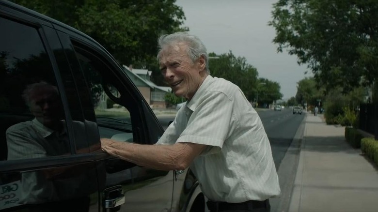 Clint Eastwood as Earl Stone in The Mule, standing next to the open window of a black truck on a neighborhood street.