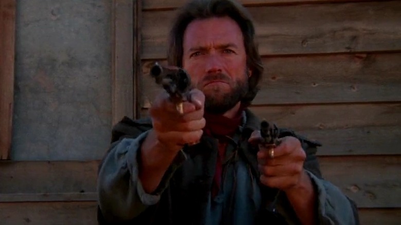 Clint Eastwood as Josey Wales in The Outlaw Josey Wales, standing in front of a building, pointing his gun off at someone.