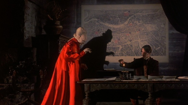 Gary Oldman as Count Dracula standing next to a table at which Keanu Reeves as Jonathan Harker is sitting in Bram Stoker's Dracula