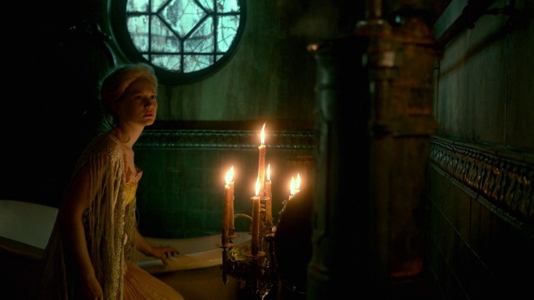 Mia Wasikowska as Edith Cushing crouching next to a candle-lit bathtub in Crimson Peak