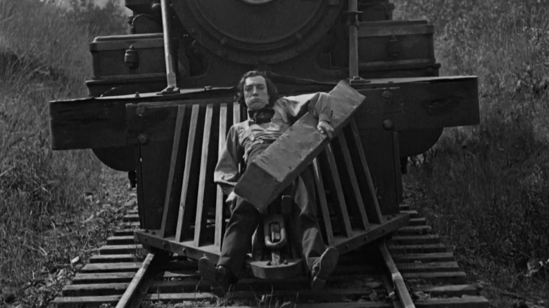 Buster Keaton as Johnnie Gray in The General, riding on the front grill of a train while holding onto a piece of railway track.