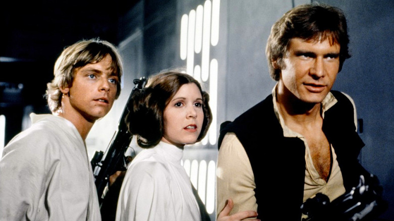 Mark Hamill as Luke Skywalker, Carrie Fisher as Princess Leia, and Harrison Ford as Han Solo, standing side by side in Star Wars.