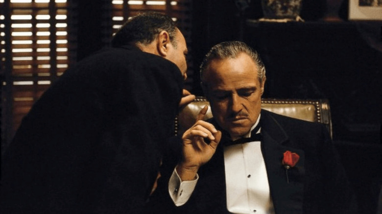 Marlon Brando as Vito Corleone listens to a man whispering in his ear in The Godfather.