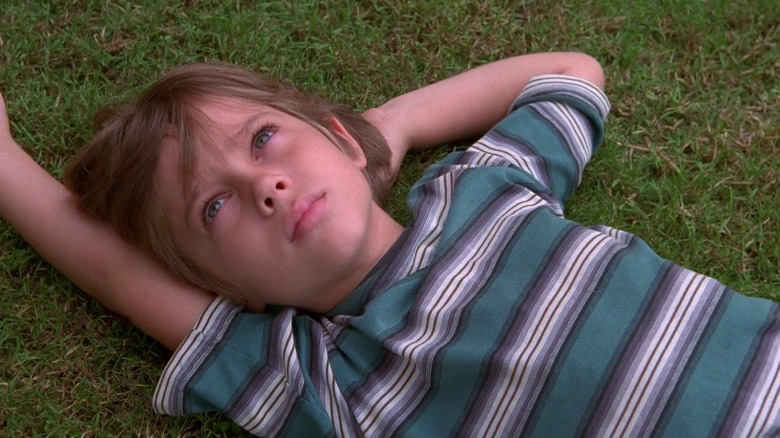 Six-year-old Ellar Coltrane as Mason laying on grass looking up in striped blue shirt in Boyhood