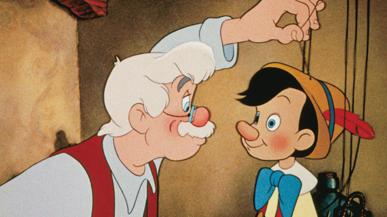 Animated Geppetto, with white hair, glasses, and red vest, holding on to string attached to Pinocchio, in brown hat with bow in his chest in Pinocchio