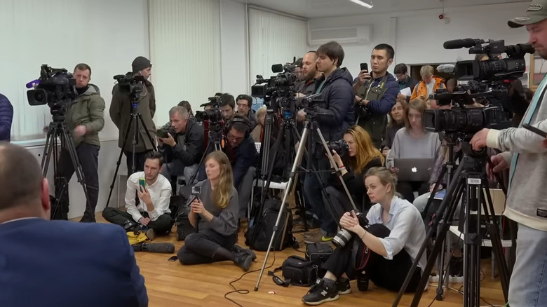 A room full of journalists aim their cameras and recorders at a table in Welcome to Chechnya