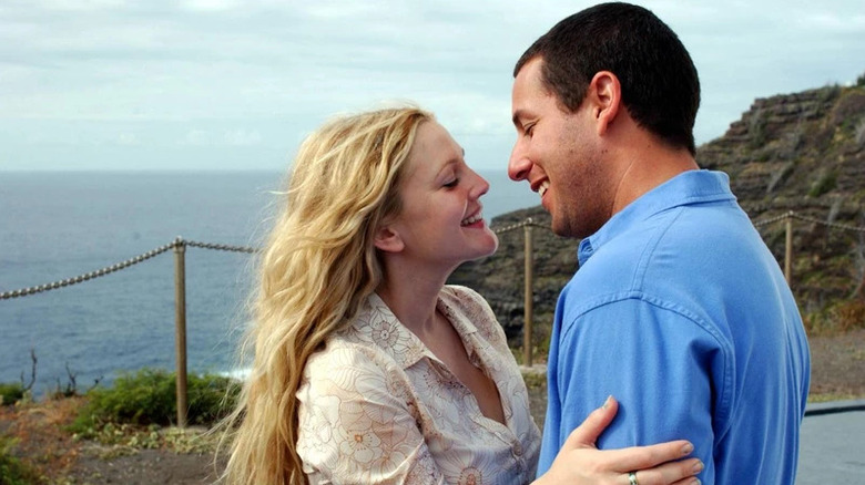 Adam Sandler as Henry Roth and Drew Barrymore as Lucy Whitmore embracing and smiling at each other with the ocean in the background in 50 First Dates.