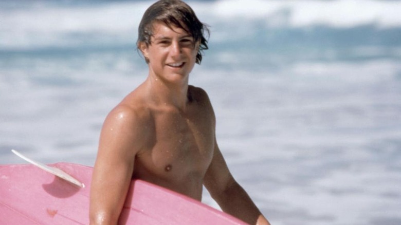 Matt Adler as Rick Kane smiling and holding a surf board in front of the ocean in North Shore.