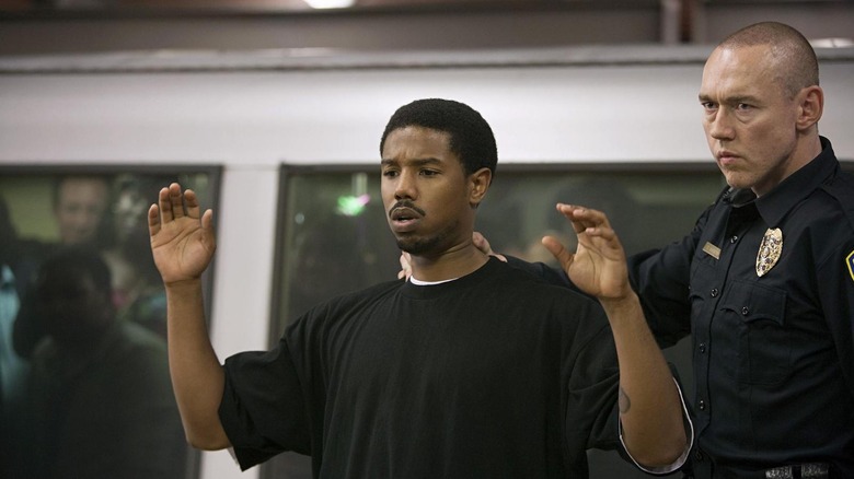 Michael B Jordan as Oscar Grant with his hands up and Kevin Durand as Officer Caruso behind him holding Oscar by the neck in Fruitvale Station