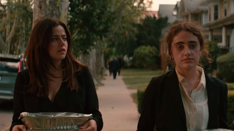 Molly Gordon as Maya walking down the sidewalk with food in trays next to Rachel Sennott as Danielle looking disheveled in Shiva Baby