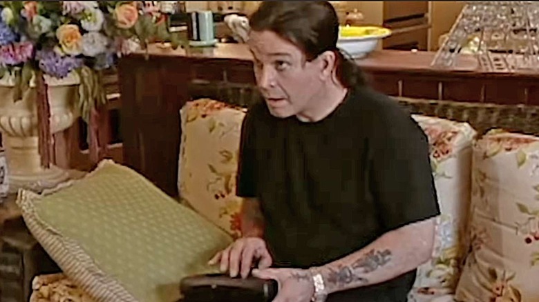 Ozzy Osbourne sits on a couch while fiddling with a gadget in The Osbournes