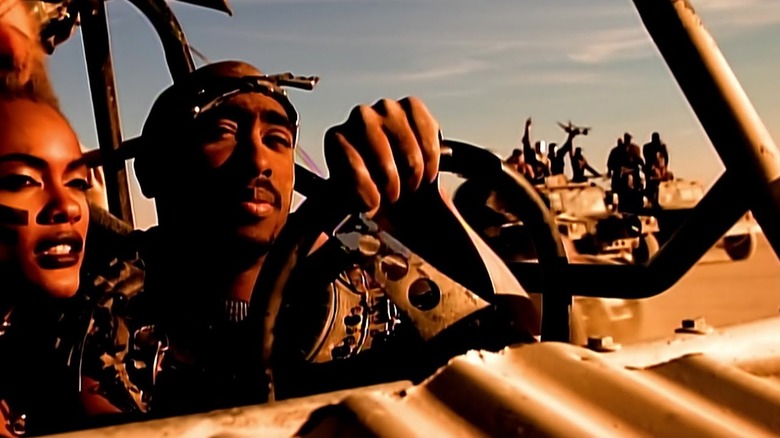 Tupac Shakur riding in a Mad Max car in a desert in the California Love music video
