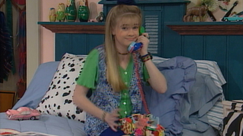 Joan Hart as Clarissa Darling in Clarissa Explains It All, sitting on her bed and holding a landline phone to her ear while looking at the camera.