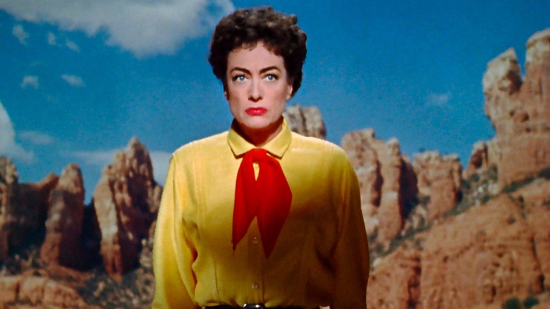 Joan Crawford as Vienna in Johnny Guitar, in a yellow button-up shirt and red neckerchief, backgrounded by a canyon.
