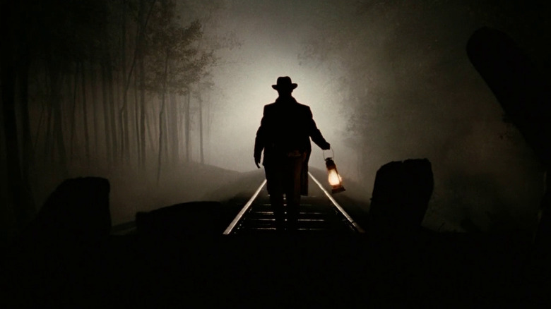 Brad Pitt as Jesse James in The Assassination of Jesse James by the Coward Robert Ford, shown in silhouette as he's lit from behind while standing on a train track in the dark and holding a lantern.