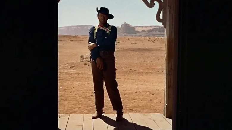 John Wayne as Ethan Edwards in The Searchers, standing alone in a doorway with the expanse of the Western landscape behind him.