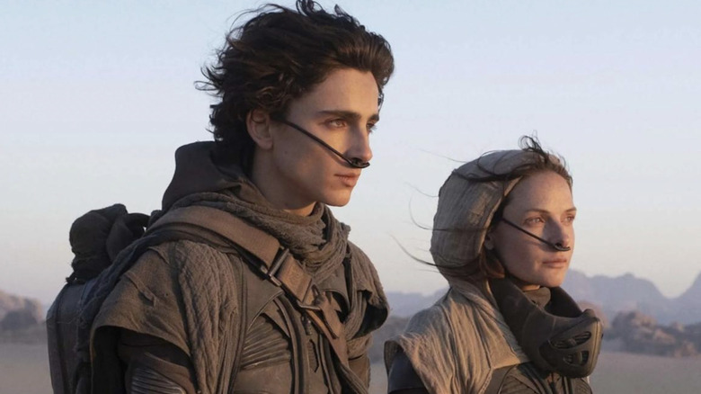 Timothée Chalamet as Paul Atreides standing next to Rebecca Ferguson as Lady Jessica wearing filt-plugs and looking off into the distance on Arrakis in Dune: Part One