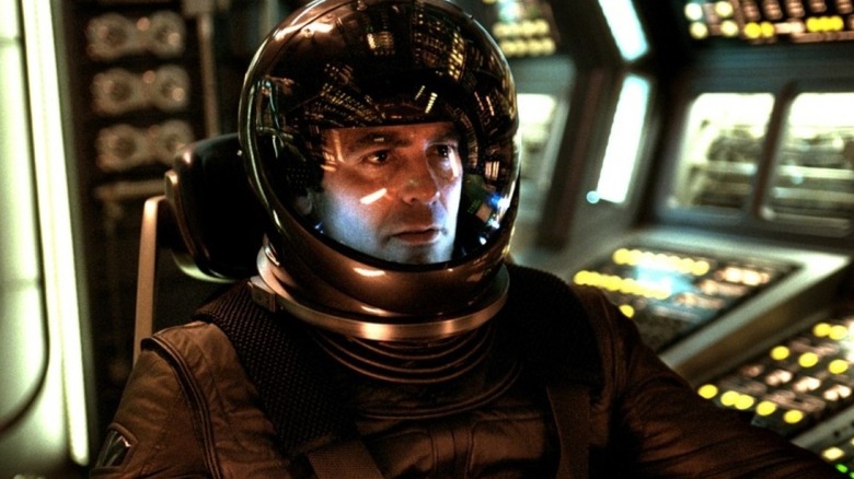 Chris Kelvin (George Clooney) sits in a control room while wearing a spacesuit in Solaris (2002)