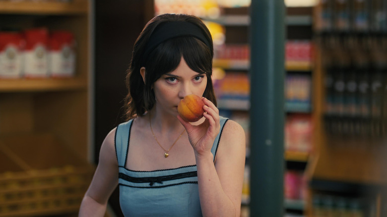 Sophie Thatcher as Iris sniffing a peach in a grocery store in Companion