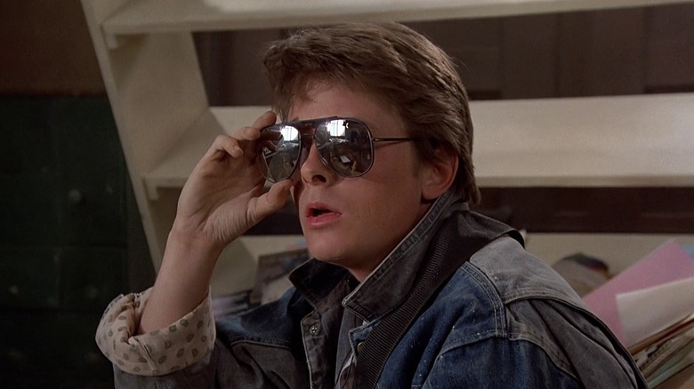 Michael J. Fox as Marty McFly in Back to the Future, looking off in the distance while taking off his sunglasses.