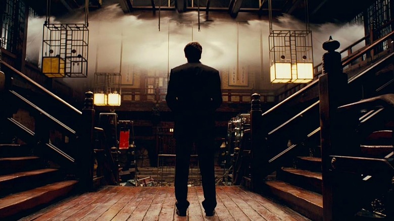 Leonardo DiCaprio as Dom Cobb in Inception, standing in a Japanese-style building where water is crashing in from the sides.