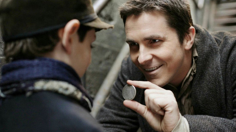 Christian Bale as Alfred Borden in The Prestige, holding up a coin to a little boy.