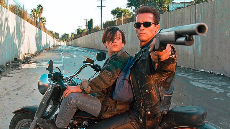 Arnold Schwarzenegger as the T-800, pointing a shotgun to protect John Connor (Edward Furlong), both on a motorcycle in Terminator 2 Judgment Day