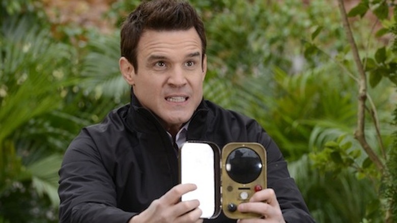 Pete Lattimer (Eddie McClintock) holds open a strange device in a jungle in Warehouse 13