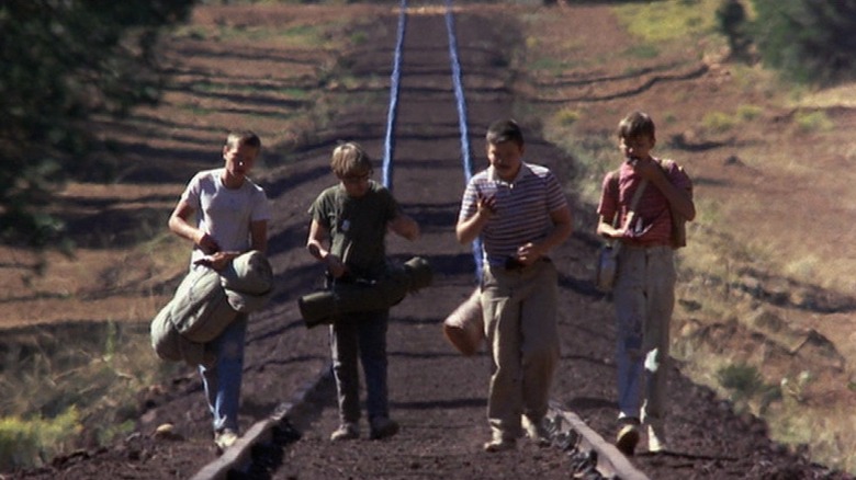 Wil Wheaton as Gordie LaChance, River Phoenix as Chris Chambers, Corey Feldman as Teddy Duchamp, and Jerry O'Connell as Vern Tessio in Stand By Me, walking alondside each other down a train track.