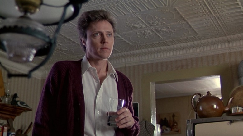 Christopher Walken as Johnny Smith in The Dead Zone, standing in a house and holding a glass of water while looking on at something out of frame.