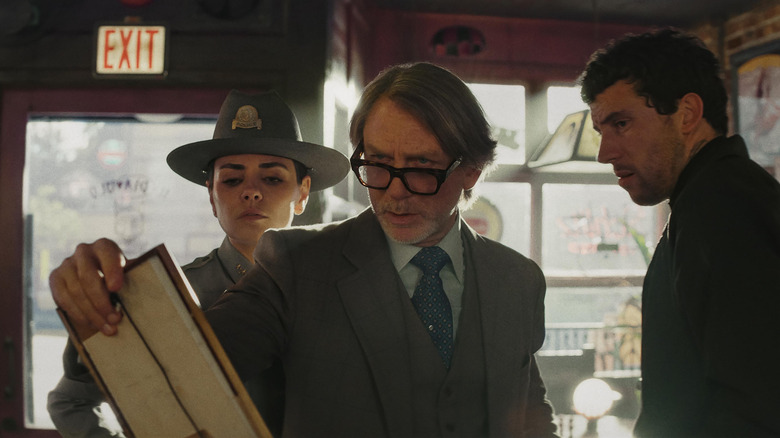 Chief Geraldine Scott, Benoit Blanc, and Jud Duplenticy looking at a picture in the bar in Wake Up Dead Man: A Knives Out Mystery