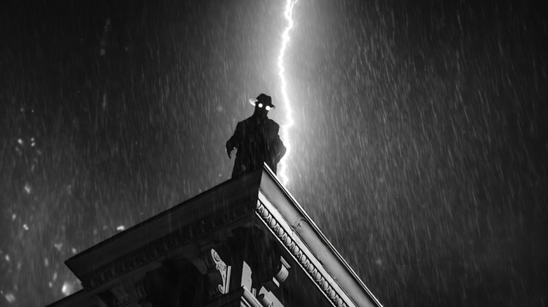 Nicolas Cage as Ben Reilly AKA The Spider in Spider-Noir, seen in silhouette with his glowing spectacles on a rooftop in the rain while lightning strikes.