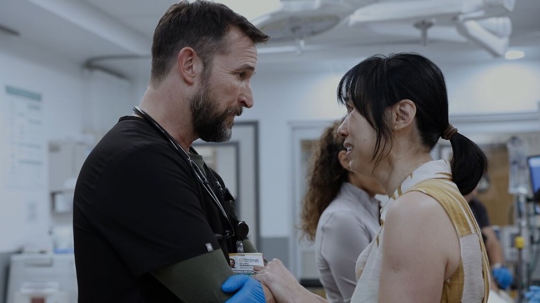Noah Wyle as Dr. Michael "Robby" Robinavitch in The Pitt, speaking with a crying woman in the hospital.