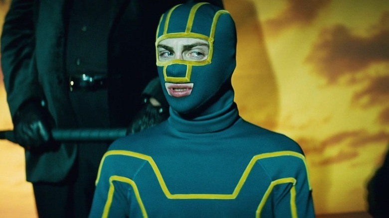 Kick-Ass (Aaron Taylor-Johnson) stands with an armed mobster behind him in Kick-Ass