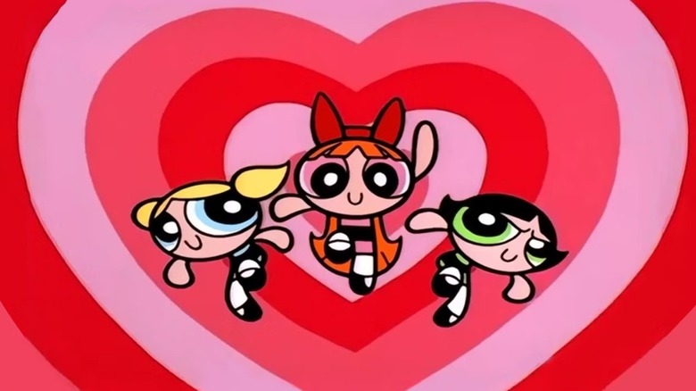 Bubbles (Tara Strong), Blossom (Cathy Cavadini), and Buttercup (E.G. Daily) fly in front of a heart-shaped background in The Powerpuff Girls