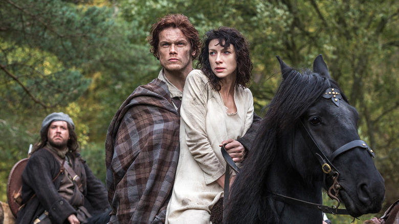 Sam Heughan and Caitríona Balfe as Jamie and Claire Fraser, riding a horse together in Outlander