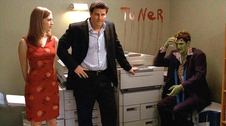 Sarah Thompson as Eve, David Boreanaz as Angel stand next to Andy Hallett as Lorne who is sitting with bloody writing above him on Angel