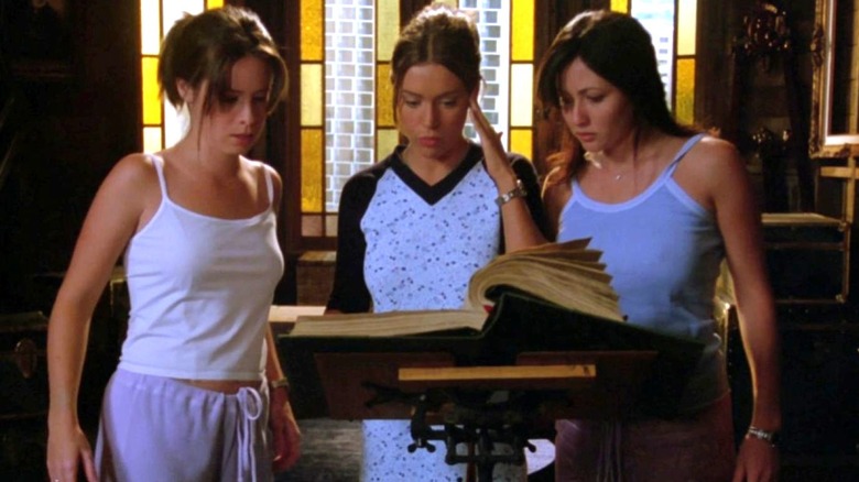 Holly Marie Combs as Piper, Alyssa Milano as Phoebe, and Shannen Doherty as Prue stand around the Book of Shadows on Charmed