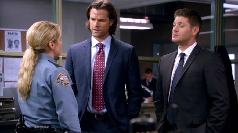 Jared Padalecki as Sam Winchester stands next to Jensen Ackles as Dean Winchester as they talk to Briana Buckmaster as Sheriff Donna Hanscum on Supernatural