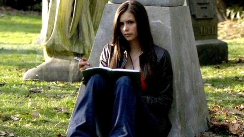 Nina Dobrev as Elena Gilbert writing in her journal while sitting in a graveyard on The Vampire Diaries