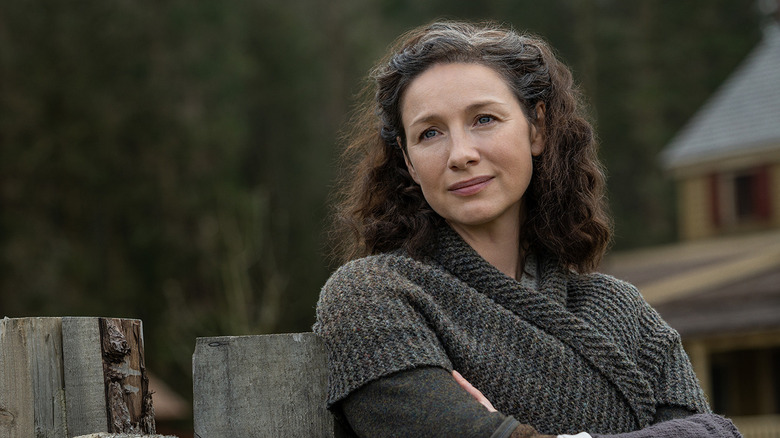 Claire Randall (Caitríona Balfe) stands with her arms crossed by a fence in Outlander