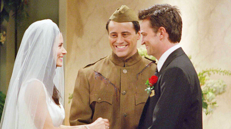 Joey Tribbiani (Matt LeBlanc) grins as Monica Geller (Courteney Cox) and Chandler Bing (Matthew Perry) exchange vows in Friends