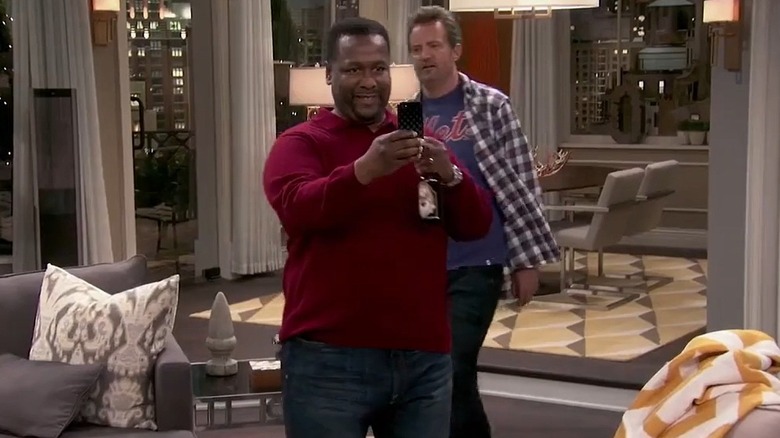 Wendell Pierce's Teddy looking at his phone in The Odd Couple