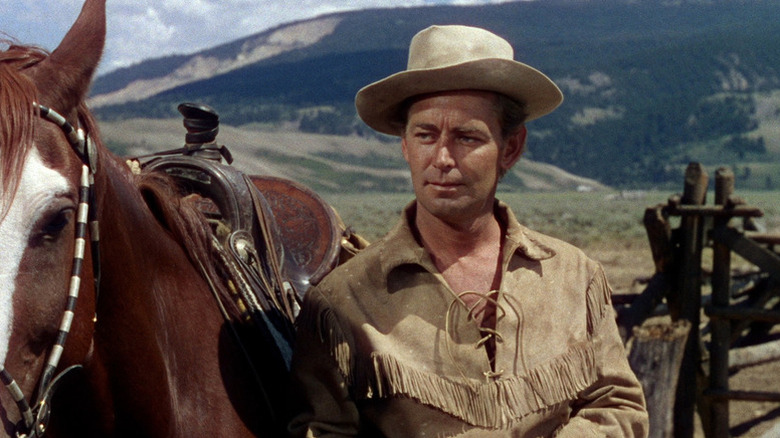 Shane (Alan Ladd) stands beside his horse in Shane